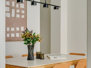 Een eetruimte met een tafel, stoelen, een vaas met bloemen, een kaars en een boek.