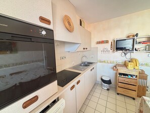 Eine kleine Küche mit Einbauofen, Spüle und einem kleinen Holzschrank.