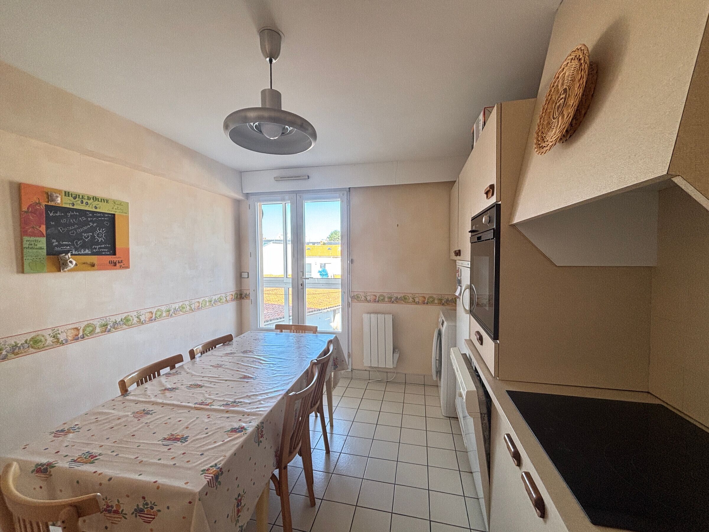 Une cuisine compacte avec une table à manger, des chaises, un luminaire suspendu et une vue par la fenêtre.