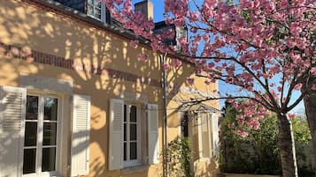 A house with a brick facade, white shutters, and a garden with blooming pink flowers.