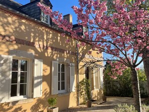 A house with a brick facade, white shutters, and a garden with blooming pink flowers.