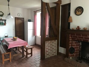 A cozy kitchen with a brick fireplace, a dining table with a checkered tablecloth, and a refrigerator.