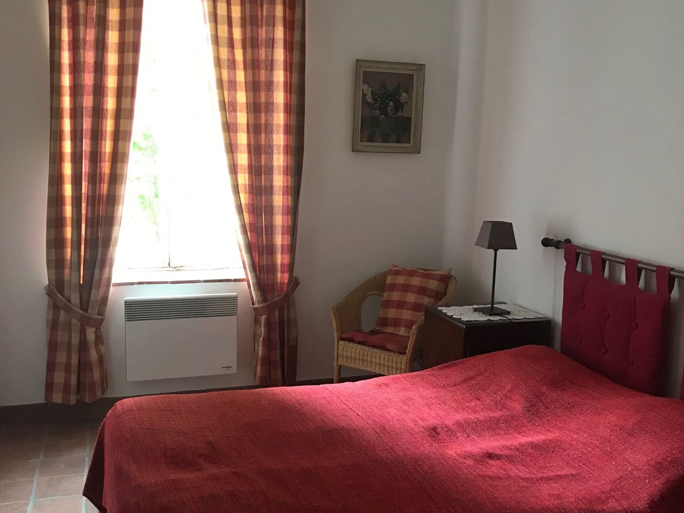 A room with a bed, a chair, a small table with a lamp, and a window with curtains.