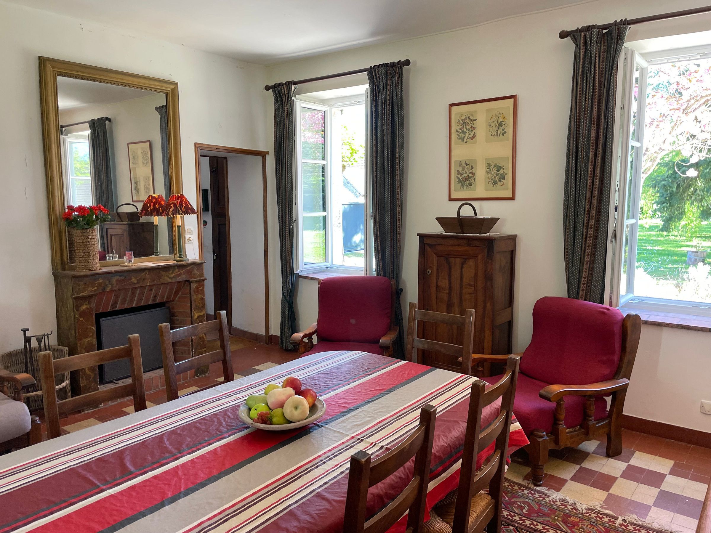A dining room with a table set for four, a fireplace, and a view of the garden through the window.