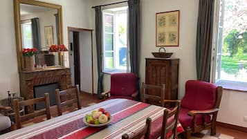 A dining room with a table set for four, a fireplace, and a view of the garden through the window.