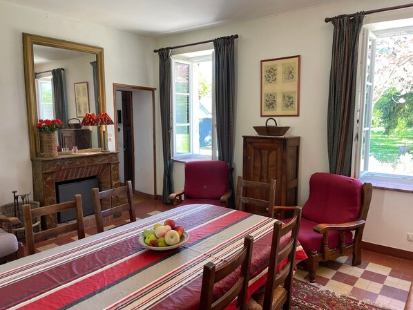 A dining room with a table set for four, a fireplace, and a view of the garden through the window.