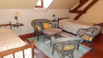 A cozy attic bedroom with a bed, two wicker chairs, a small table, and a window.