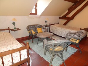 A cozy attic bedroom with a bed, two wicker chairs, a small table, and a window.