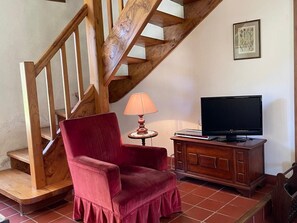 A staircase with wooden railings, a red upholstered chair, a small table with a lamp, and a television on a wooden cabinet.