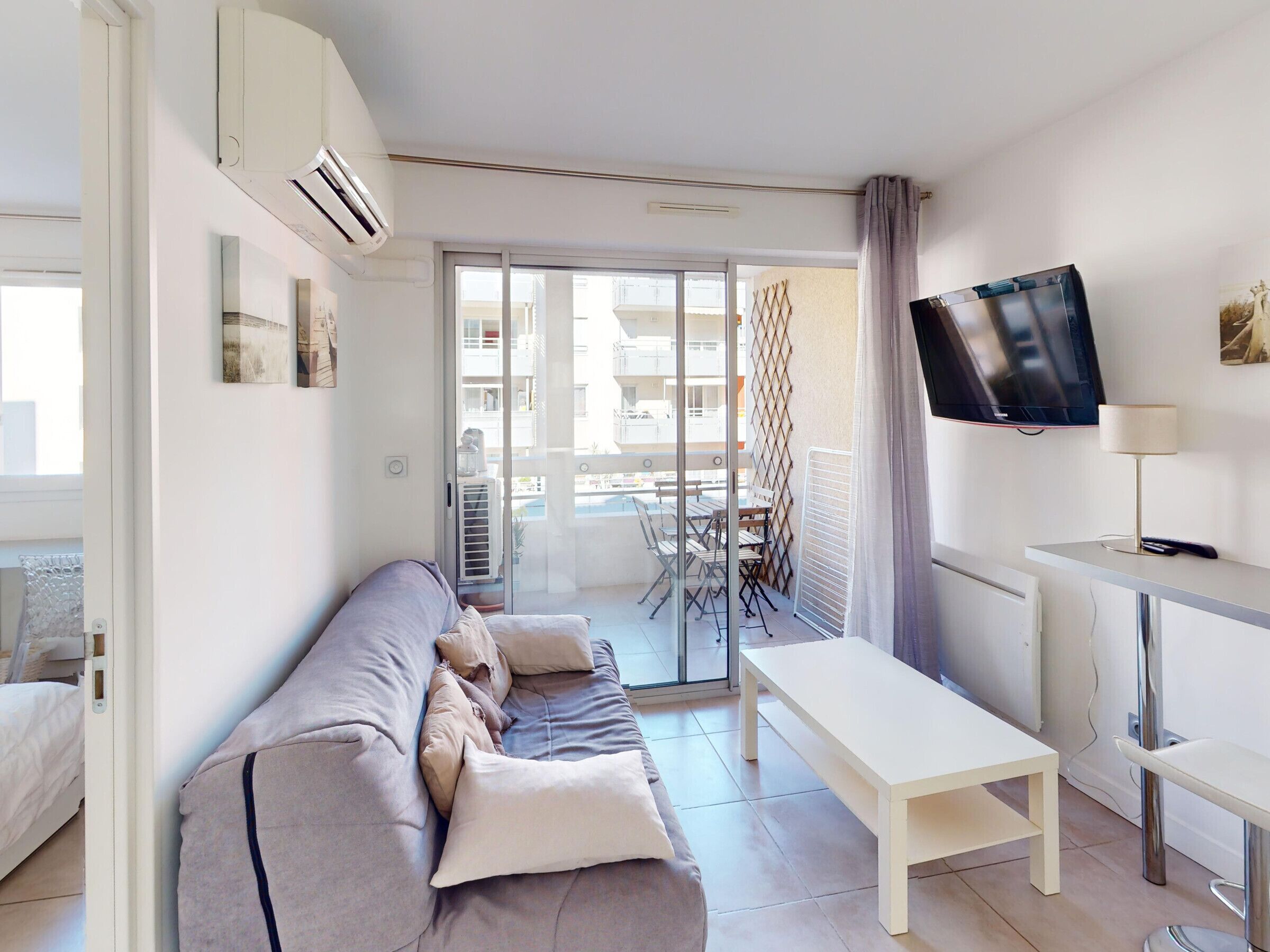 Un salon moderne avec un canapé, un téléviseur et un balcon équipé d’une table et de chaises.