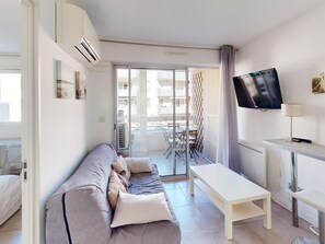 A modern living room with a sofa, a TV, and a balcony with a table and chairs. - Apartment with AC - Discover Sète (Sète)