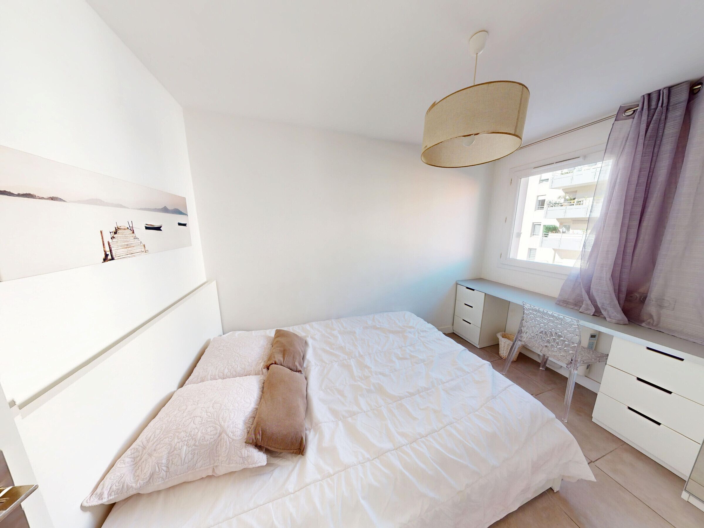A bedroom with a bed, a desk, and a window with curtains.