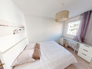 A bedroom with a bed, a desk, and a window with curtains. - Apartment with AC - Discover Sète (Sète)