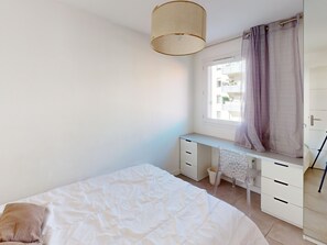 Et soveværelse med en seng, et skrivebord og et vindue med gardiner.
