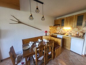 Un comedor con mesa y sillas de madera, una cocina con armarios de madera, salpicadero de azulejos e iluminación colgante.