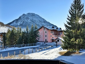 Un edificio de varios pisos con el suelo cubierto de nieve, rodeado de árboles de hoja perenne y una montaña al fondo.