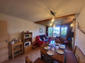 Un'accogliente zona giorno con tavolo da pranzo per quattro persone, un divano rosso e una libreria in legno.