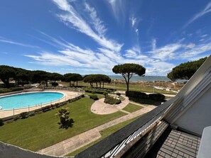 A swimming pool surrounded by a well-maintained lawn, with a clear view of the sea and a large tree in the background. - Apartment with AC and sea view - 4/5 guests (Port Camargue)