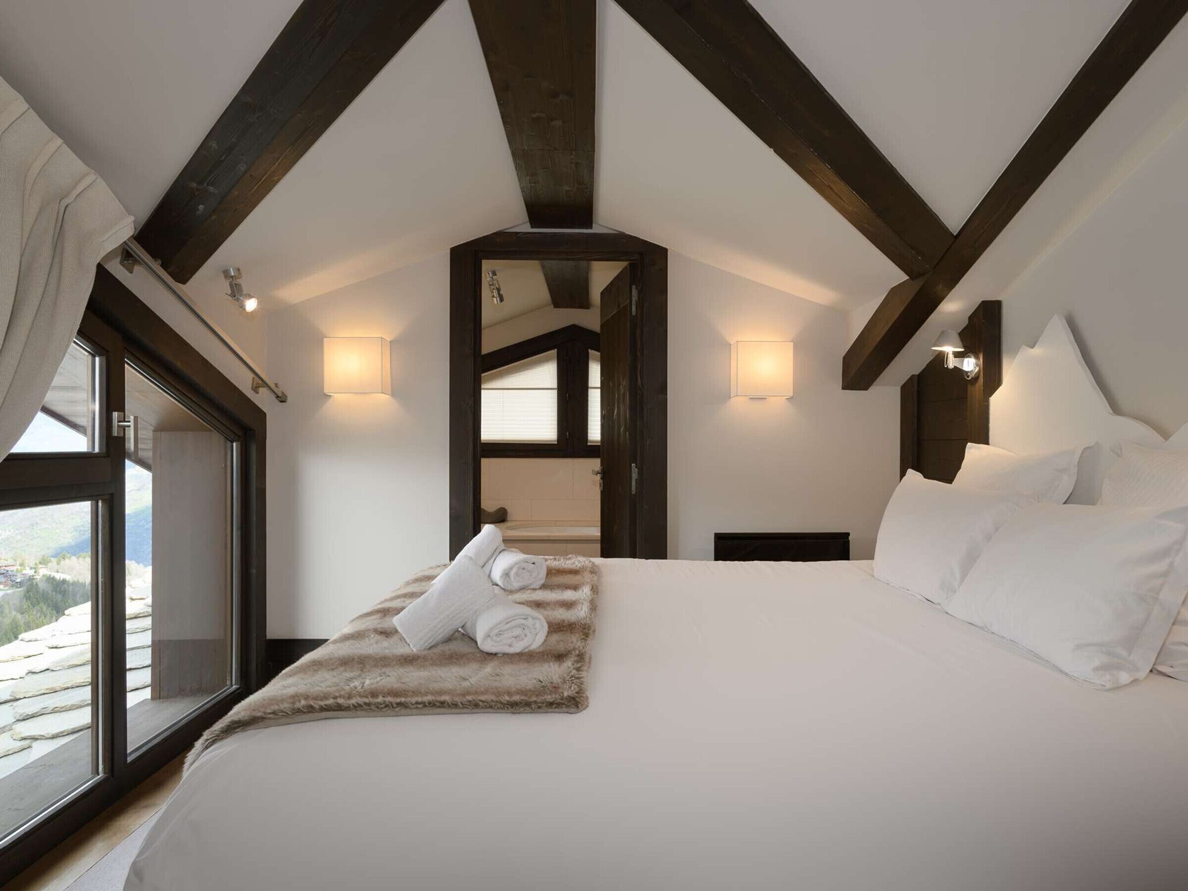 A bedroom with a large bed, a window, and a view of the mountains.