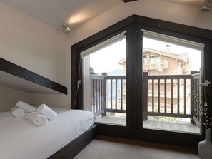 A bedroom with a large window, a bed with white linens, and a view of a building outside. - Duplex apartment in the center - 8 guests (Courchevel 1650)