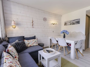 Ein modernes Wohnzimmer mit einer Couch, einem Esstisch mit Stühlen, einem kleinen Beistelltisch und einer Wandleuchte.