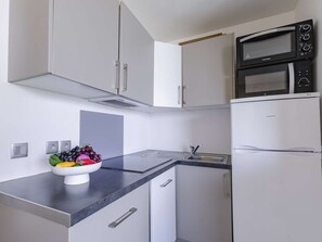 Eine moderne Küche mit weißen Schränken, einer schwarzen Mikrowelle, einem eingebauten Backofen und einer Schüssel Obst auf der Arbeitsfläche.