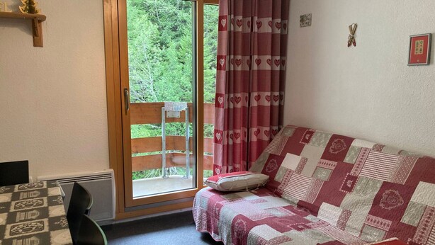A cozy room with a wooden bench outside a sliding glass door, a quilted sofa with pillows, and a patterned rug. - Apartment 4 guests, slope view - Le Pleynet (Le Pleynet)