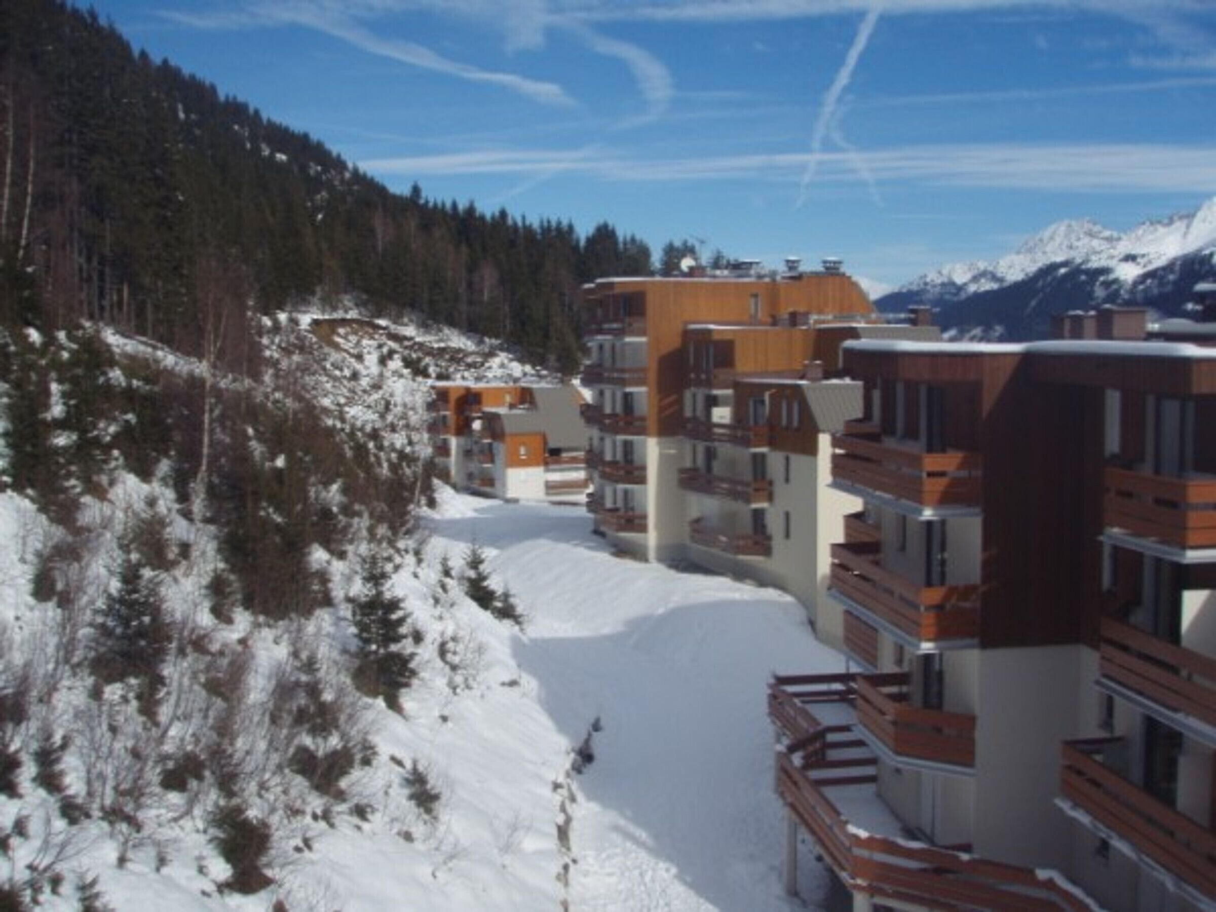A row of modern multi-story buildings with balconies, set against a snowy mountain backdrop.