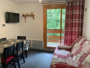 Une pièce comprenant une table à manger, des chaises, un canapé, un téléviseur fixé au mur et une porte-fenêtre coulissante donnant sur un espace extérieur.