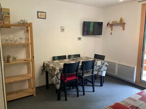 A dining area with a table set for four, surrounded by chairs, a wooden shelf with glassware, and a television mounted on the wall. - Apartment 4 guests, slope view - Le Pleynet (Le Pleynet)