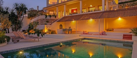 A large house with a swimming pool, outdoor seating, and a staircase leading to a balcony.