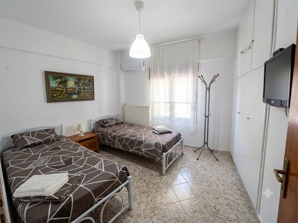 Un dormitorio con dos camas, una lámpara de pie, un televisor y un cuadro en la pared.