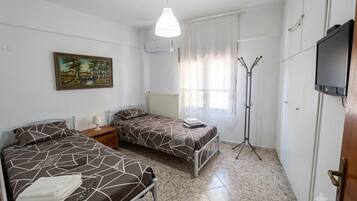 Un dormitorio con dos camas, una lámpara de pie, un televisor y un cuadro en la pared.