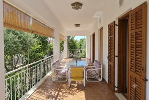 A balcony with a table and chairs, a white railing, and a view of greenery. - Kostas's House (Serraiki Akti)