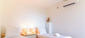 Une chambre d’hôtel avec un lit, des lampes de chevet, une table de chevet, un climatiseur fixé au mur et une petite statue posée sur une étagère.
