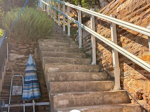 Un escalier en pierre avec des rampes en métal, une échelle en métal et un tissu rayé accroché au mur.