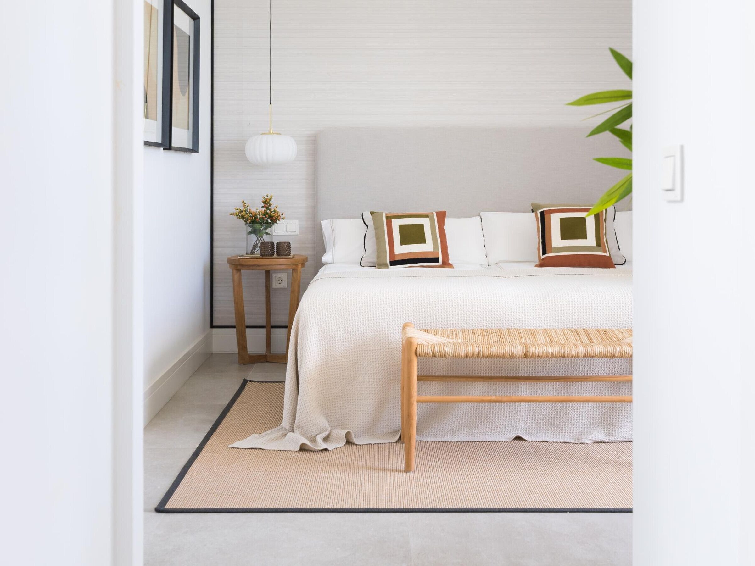 A bedroom with a bed, bedside table, lamp, and a bench.