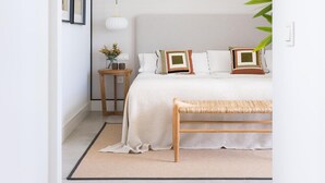 Een slaapkamer met een bed, nachtkastje, lamp en een bankje.