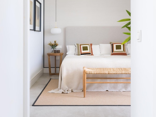 A bedroom with a bed, bedside table, lamp, and a bench.