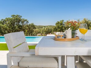 A white outdoor table with a chair, a pitcher, a glass of orange juice, and a vase with flowers.
