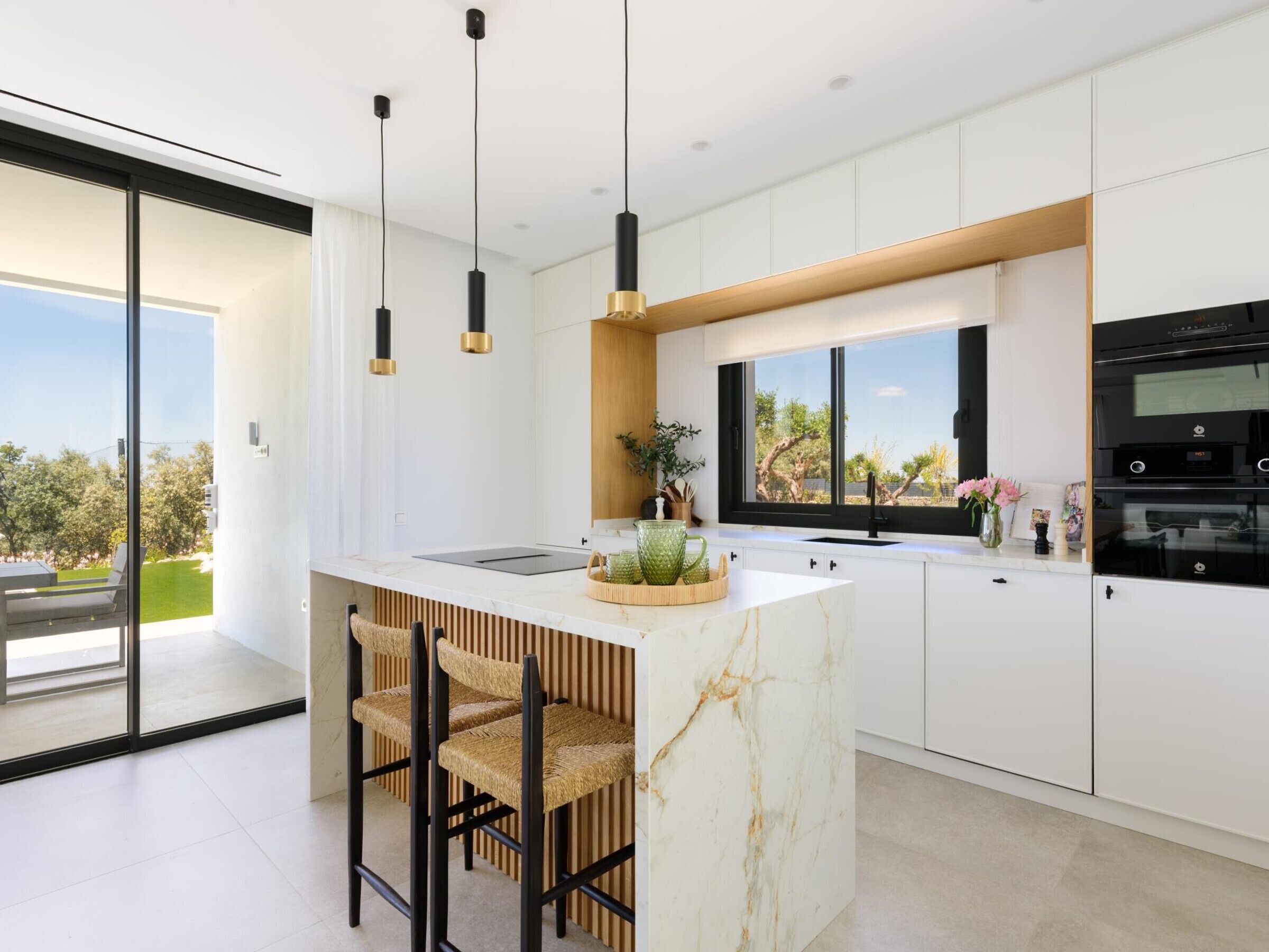 Une cuisine moderne dotée d’un îlot central, de tabourets de bar, de luminaires suspendus et offrant une vue sur l’extérieur.
