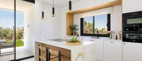 A modern kitchen with a central island, bar stools, pendant lighting, and a view of the outdoors.