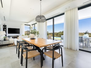 A modern dining area with a wooden table and chairs, a large window with a view of the outdoors, and a television on the wall. - Luxurious villa with private pool in Antequera (Antequera)