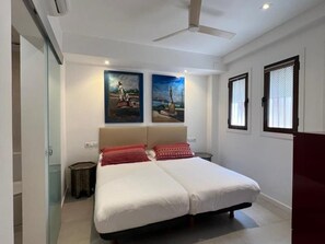 A double bed with a headboard, two wall-mounted paintings, a ceiling fan, and a window with blinds. - Central apartment in Málaga - 2 guests (Málaga)