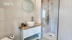 A modern bathroom with a round mirror, a sink, and a glass-enclosed shower. - Central apartment in Málaga - 2 guests (Málaga)