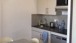 A compact kitchen with a sink, microwave, and dishwasher. There are chairs and a table in the foreground. - Apartment with air conditioning, lake view - 4 guests (Le Barcarès)