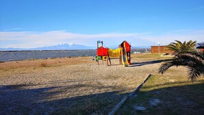 A playground with a slide and climbing structure near a beach with a mountain backdrop. - Apartment with air conditioning, lake view - 4 guests (Le Barcarès)