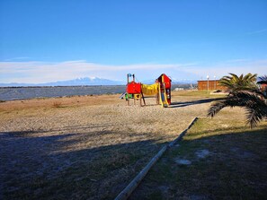 Ein Spielplatz mit Rutsche und Klettergerüst in der Nähe eines Strandes, vor einer Bergkulisse.