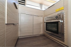A compact kitchen with a built-in oven and a microwave, wooden cabinetry, and a ceiling vent.