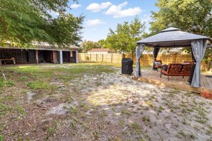 Un patio trasero con terraza techada, una parrilla y mobiliario exterior.